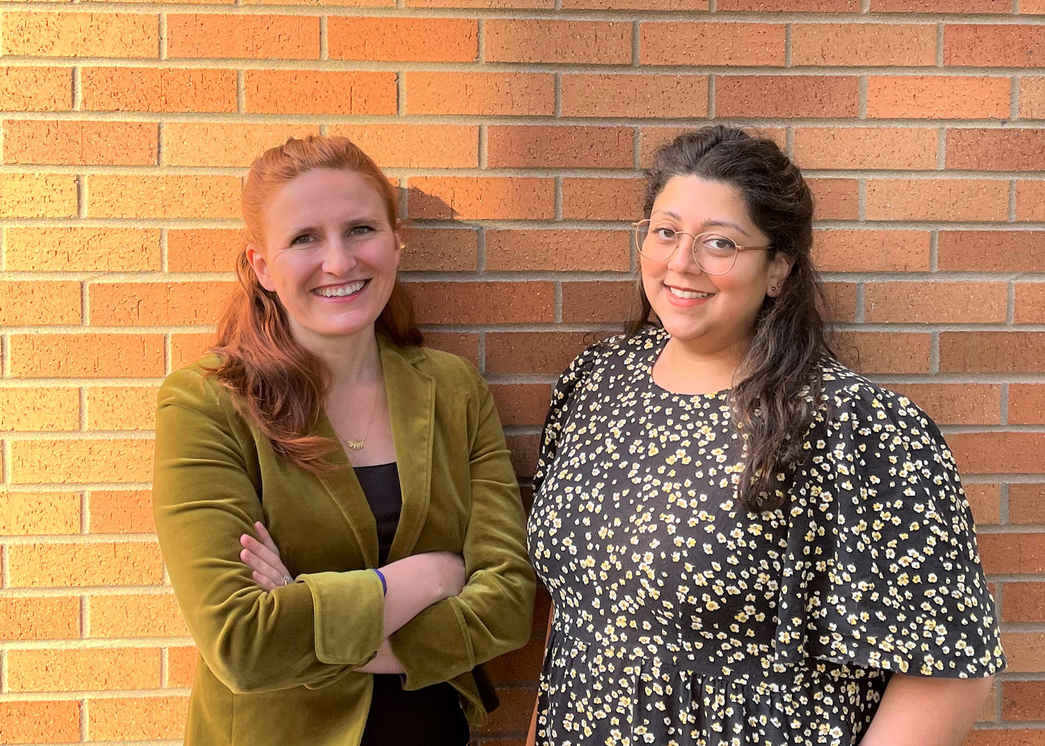 Lily and Monika, co-founders, stand in front of a brick wall on a sunny day.